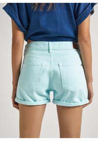 Pantalones cortos de mezclilla azul claro con puños doblados, que presentan dos bolsillos traseros y una etiqueta de cuero marrón en la cintura. Diseño simple y casual.