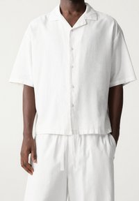 Wit overhemd met korte mouwen en knopen, een campkraag, lichtgewicht stof, rechte snit, subtiele textuur en transparante knopen.