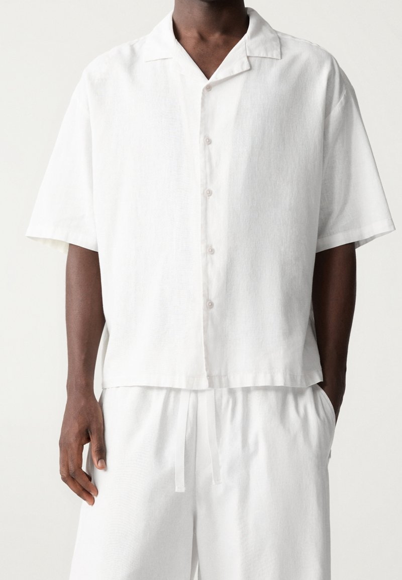 Wit overhemd met korte mouwen en knopen, een campkraag, lichtgewicht stof, rechte snit, subtiele textuur en transparante knopen.