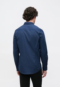Hosszú ujjú ing tengerészkék anyagból, finom textúrával, gombos mandzsettával és ívelt aljú kialakítással. Hátsó nézet.