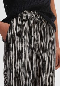 Zwart-wit gestreepte broeken met een ruime pasvorm, voorzien van een elastische tailleband met een trekkoord en zijzakken. Gemaakt van lichte stof.