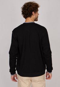 Sweatshirt noir à manches longues, avec des poignets et un ourlet côtelés, et un col rayé contrastant. Le tissu semble doux avec une texture lisse.