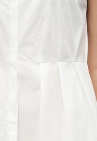 Λευκό αμάνικο φόρεμα με κάθετες και οριζόντιες ραφές, που δείχνει μέρος του κορμού και του δεξιού βραχίονα.