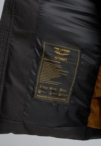 Gevoerde pufferjack met een wollenachtige buitenkant, zwarte stof en gouden binnenkant. Laat het waslabel zien met productspecificaties en logo's.
