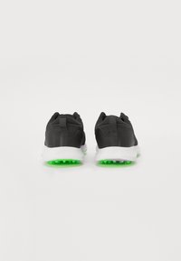 Black sneakers with mesh fabric, white midsoles, and green rubber outsoles. Features a textured design and pull tab at the heel.