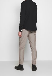 Czarna koszula zapinana na guziki w połączeniu z jasnoszarymi dopasowanymi spodniami i czarnymi botkami, prezentująca prosty, elegancki design.