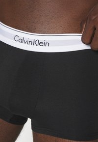 Sorte bomullstruser med tettsittende passform, med en hvit elastikk med svart "Calvin Klein"-logo og kontrastsøm langs kantene.