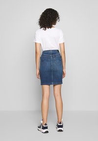 Jeanskjol med figurnära passform, midja-till-lår längd, mörkblå färg, och två bakfickor. Kombinerad med en vit T-shirt och sneakers.