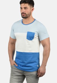 Blå og hvit fargeblokkert t-skjorte med rund hals, kort erme og en liten brystlomme. Laget av mykt stoff.