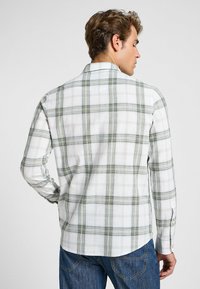 Camicia bianca a maniche lunghe con motivo a quadri verdi, polsini con bottone e orlo arrotondato. Realizzata in tessuto leggero e traspirante.