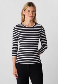 Langärmliges, geripptes Oberteil mit navy-blauen und weißen Streifen, Rundhalsausschnitt und Dreiviertelärmeln, kombiniert mit schwarzen, taillierten Hosen.