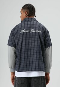 Donker geruit overhemd met korte mouwen en grijze mouwen, met "Saint Essence" in het wit geborduurd op de rug. Casual pasvorm, lichtgewicht stof.