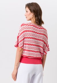 Gebreide trui met een zigzagpatroon in roze en wit, korte mouwen en een effen roze geribbelde zoom. Soepele textuur en een comfortabele pasvorm.