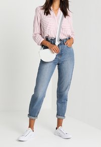 Blusa a righe rosa chiaro con maniche lunghe, jeans in denim blu a vita alta, borsa a tracolla bianca e sneakers bianche.