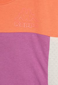 Camiseta de color bloqueada con secciones en naranja, púrpura y blanca, hecha de una tela suave. Logo de Kappa en textura elevada en el pecho.