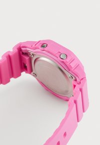 Montre en silicone rose vif avec un dos en acier inoxydable rond, texture lisse et deux boutons argentés sur le côté.