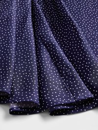 Marineblauer Stoff mit weißen Punkten, glatte Textur, gefaltet, um den Fall zu zeigen. Die Kanten sind ordentlich gesäumt, was ein leichtes Design zeigt.