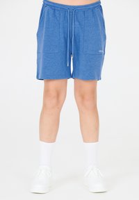 Siniset puuvillasekoiteshortsit, joissa on joustava vyötärönauha, kiristysnauha ja kaksi etutaskua. Tyylinä valkoiset tennarit ja sukat.