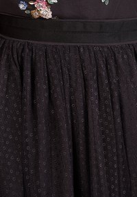 Jupe en tulle noire avec une surface texturée, dotée d'une ceinture ajustée et de broderies florales avec des paillettes en rose, bleu et blanc.