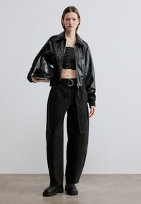 Μαύρο δερμάτινο σακάκι cropped πάνω από μαύρο cropped τοπ με κουμπιά, σε συνδυασμό με φαρδιά μαύρη παντελόνα και χοντρά μαύρα παπούτσια με πλατφόρμα.