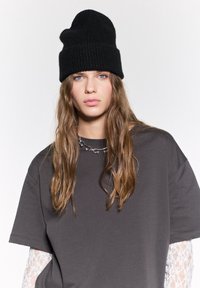 Beanie nero in maglia e T-shirt grigia oversize con dettagli in pizzo sulle maniche, caratterizzata da un collo rotondo e una vestibilità comoda.