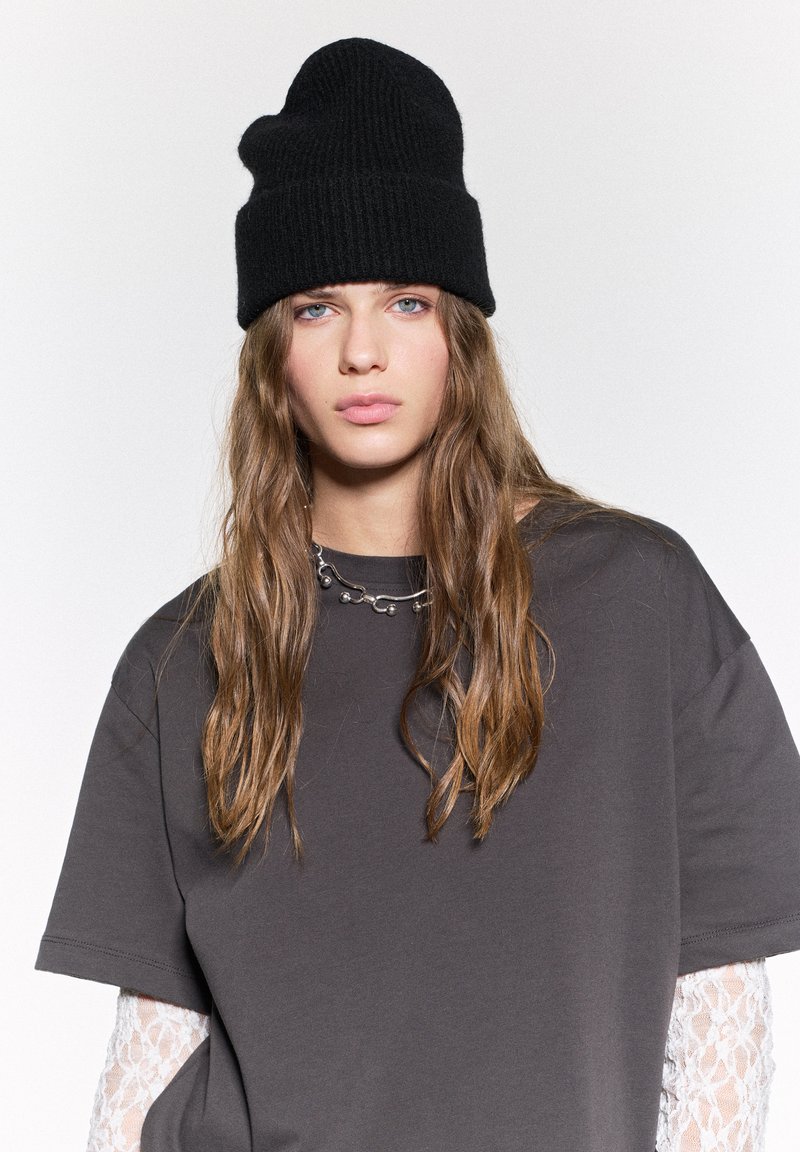 Beanie nero in maglia e T-shirt grigia oversize con dettagli in pizzo sulle maniche, caratterizzata da un collo rotondo e una vestibilità comoda.