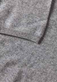 Tissu tricoté gris doux avec un poignet côtelé replié, montrant la texture et les détails du fil fin.