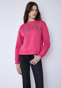 Rosa Sweatshirt mit Leopardenmuster und "MILANO" Schriftzug, Rundhalsausschnitt und gerippten Bündchen, kombiniert mit schwarzen Jeans. Weicher Stoff, lässige Passform.