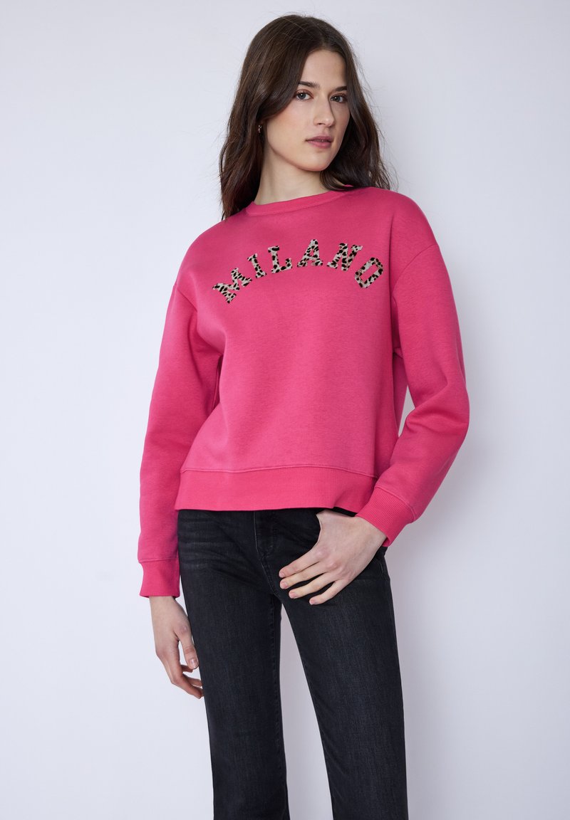Rosa Sweatshirt mit Leopardenmuster und "MILANO" Schriftzug, Rundhalsausschnitt und gerippten Bündchen, kombiniert mit schwarzen Jeans. Weicher Stoff, lässige Passform.
