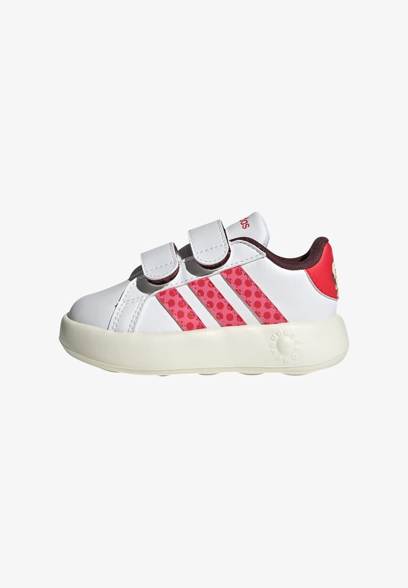 Baskets blanches pour enfants avec des accents rouges et trois bandes roses à pois. Elles sont dotées de straps Velcro et d'une semelle ronde pour un bon soutien.