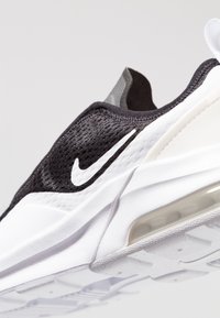 Černobílá Nike teniska s texturovaným svrškem, bílou mezipodešví a viditelným vzduchovým polštářem. Má výrazné logo swoosh.