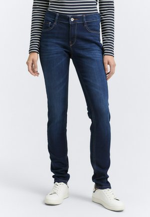 Tmavomodré denimové džiny so slim fit strihom, vysokým pásom, jemným prešitím a prednými vreckami, skombinované s bielymi teniskami.