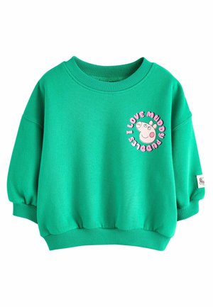 Sweatshirt vert avec un col rond, des manches bouffantes et un graphique circulaire représentant un cochon avec le texte "J'aime les flaques de boue."