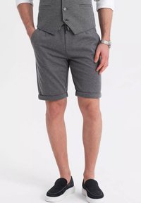 Shorts grigi con texture e orlo arrotolato, dotati di tasche laterali e vestibilità comoda, abbinati a scarpe nere senza lacci.
