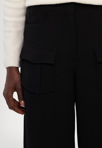 Zwarte cargobroeken hebben twee grote klepzakken aan de zijkanten, een gladde textuur en een aansluitende tailleband voor een gestroomlijnde uitstraling.