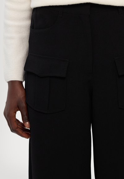 Black cargo pants feature two large flap pockets on the sides, a smooth texture, and a fitted waistband for a streamlined look.