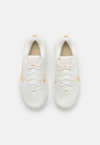 Hvide atletiske sko med en tekstureret overdel, beige detaljer, guld Swoosh-logo og hvide snørebånd, der har en afrundet tå og polstret sål.
