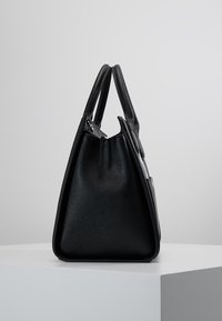 Mustakotoinen nahkalaukku, jossa on rakenteellinen, kolmiomainen muoto. Siinä on kaksi lyhyttä kahvaa ja teksturoidun pinnan viimeistely, sekä kääntölaippa ja hopeiset yksityiskohdat.