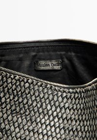 Czarna torba o teksturowanym splocie z metalowym zamkiem. Wewnątrz widoczna czarna podszewka oraz metka z logiem "Massimo Dutti."