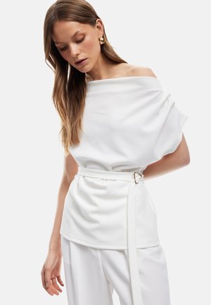Witte off-shoulder top van zachte, gedrapeerde stof, met een ceintuur op de taille en een gouden hardware accent; gecombineerd met bijpassende broek.
