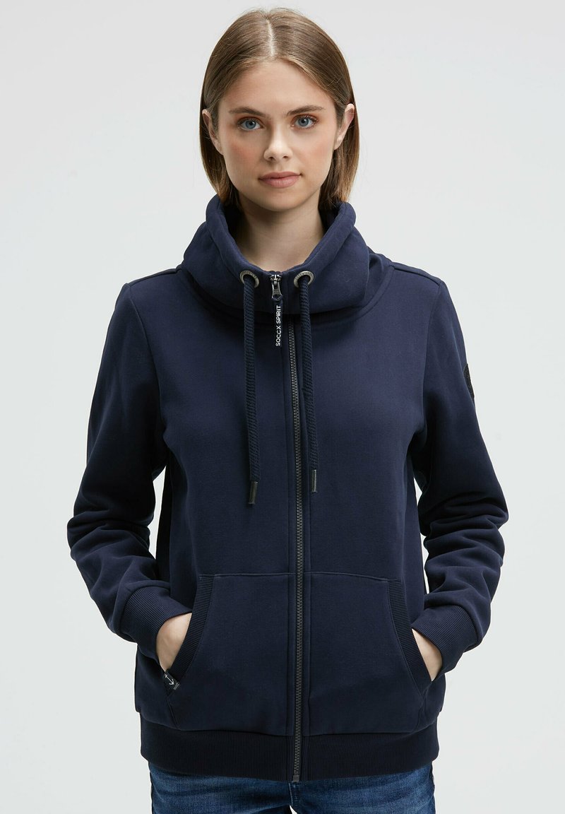 Navy zip-up hoodie with a high collar, drawstrings, two front pockets, and ribbed cuffs. Made from soft fabric, featuring a smooth texture.