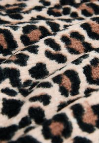 Tissu doux avec motif léopard marron, noir et beige, montrant des plis et des détails de texture.