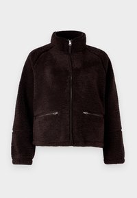 Giacca in pile nera con colletto alto, chiusura con zip frontale e due tasche con zip. Presenta un tessuto morbido e testurizzato e un design corto.