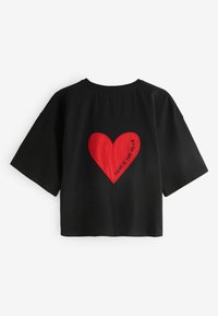 Čierne tričko s krátkym rukávom s veľkou červenou aplikáciou srdca na chrbte, s textom "LOVE IS THE DRUG" vyšitým čiernou niťou.