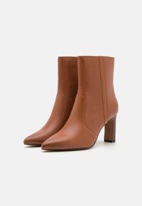 Brune skinn ankelstøvler med spiss tå, sidesømmer og blokk-hæl, med en glatt tekstur og minimalistisk design.