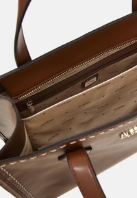 Borsa tote in finta pelle marrone con finitura liscia, dotata di una tasca con zip e fodera interna con motivo stampato "GUESS".