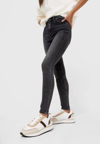 Jeans ajustados negros con cintura alta, que cuentan con dos bolsillos delanteros. Combinados con zapatillas blancas y beige y un suéter ligero.