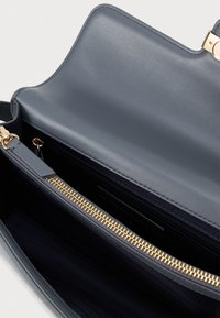 Sötétkék bőrtáska sima textúrával. Arany cipzárral és fém kiegészítőkkel rendelkezik. A belső térben cipzáras zseb és textilbélés található.