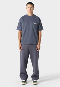 T-shirt oversized gris foncé avec une petite poche poitrine et un détail graphique, associé à un pantalon de survêtement gris assorti et des baskets noires.