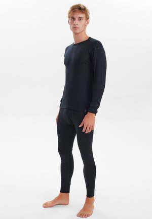 Sort langærmet termotrøje kombineret med sorte tætsiddende leggings lavet af et glat, strækbart materiale. Har rene linjer og tætsiddende manchetter.